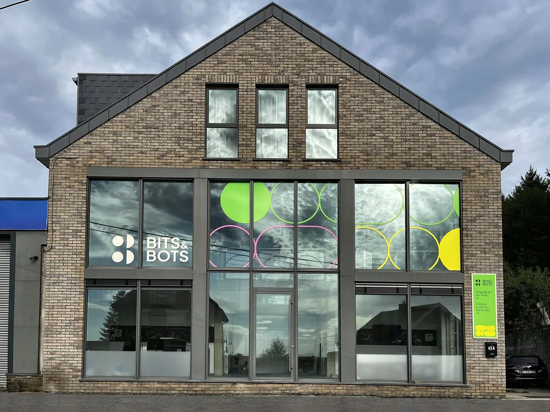 Das Bürogebäude von Bits & Bots in Kelmis, mit Logo und farbigen Kreisen auf der Glasfassade